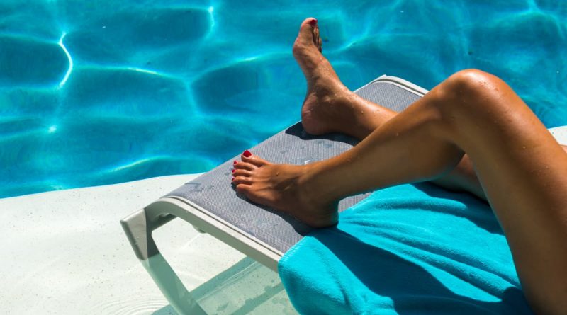 Fotografia delle gambe abbronzate di una donna sdraiata su un lettino accanto ad una piscina